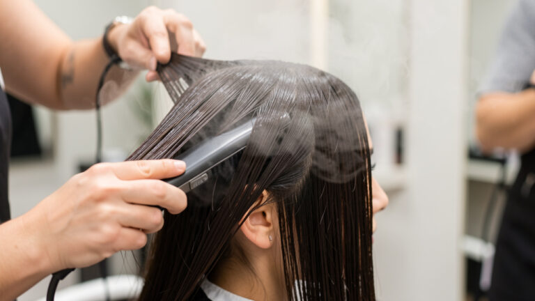 Gros plan d’une femme dont les cheveux sont lissés avec un appareil diffusant une fine vapeur chaude dans un salon de coiffure.